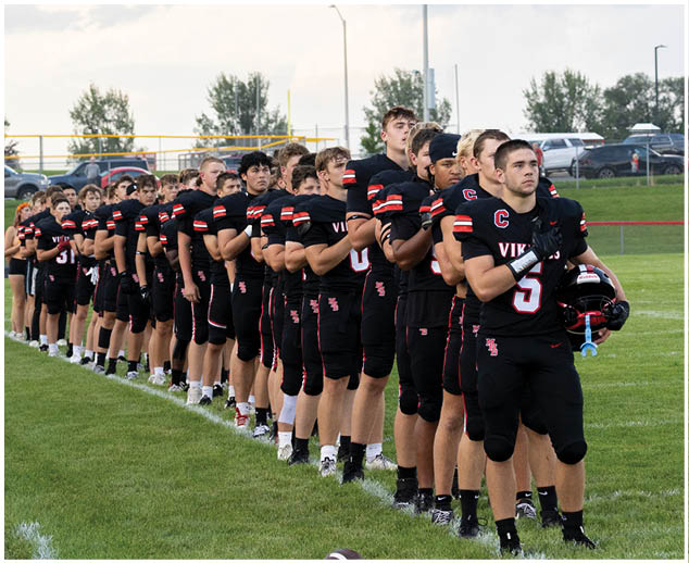 A group of football players in black uniforms standing on a field. Description generated by AI