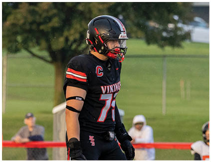 A football player wearing a black jersey with the number 77 on it. Description generated by AI