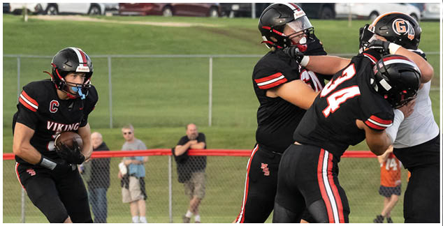 A football player in a black jersey is tackled by another player. Description generated by AI