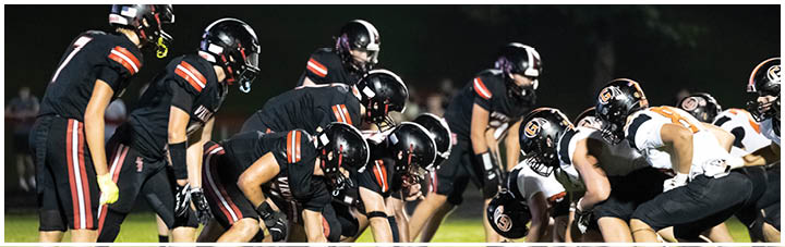 A group of football players in black and orange uniforms are on the field. Description generated by AI