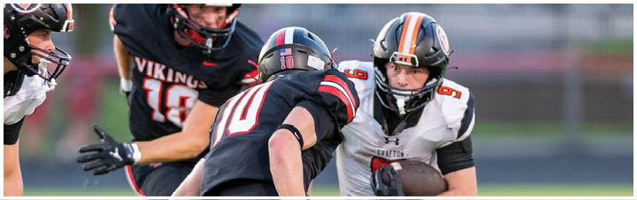 A football player in a black jersey is tackled by another player. Description generated by AI