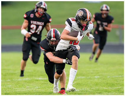 A football player in a black jersey is tackled by another player. Description generated by AI