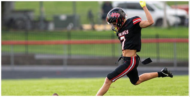 A football player in a black and red jersey kicks a football. Description generated by AI