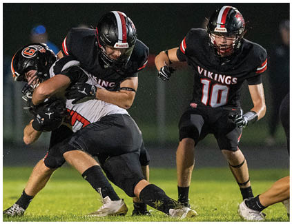 A football player in a black and white jersey is tackled by another player. Description generated by AI