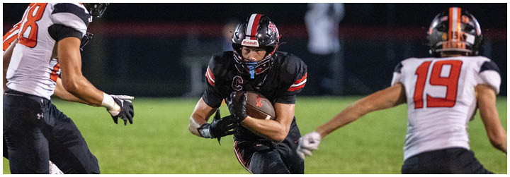 A football player in a black jersey is running with a football. Description generated by AI