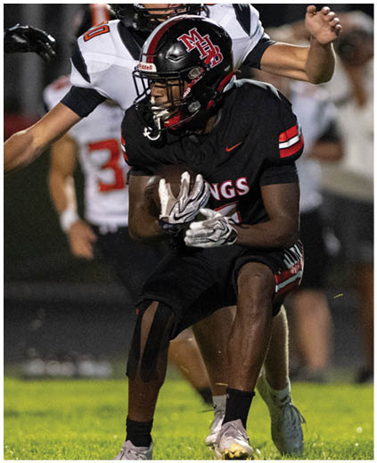 A football player in a black jersey is running with the ball. Description generated by AI