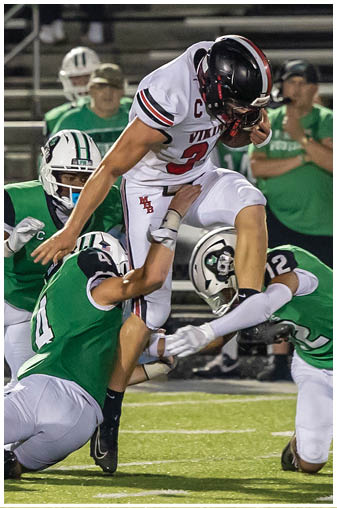A football player in a green jersey is tackled by another player. Description generated by AI