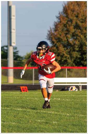 A football player in a red jersey running on the field. Description generated by AI