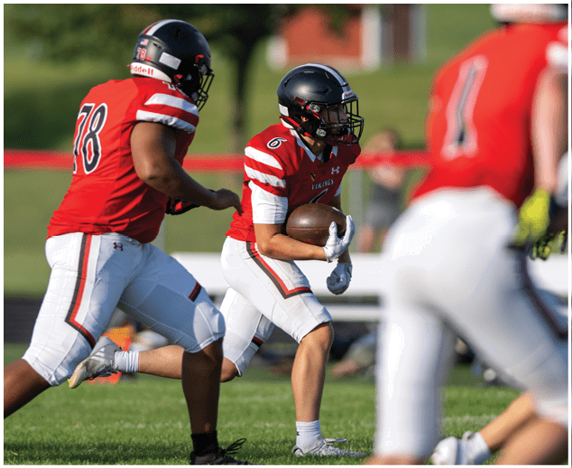 A football player in a red jersey is running with the ball. Description generated by AI
