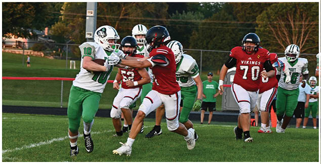 A football game is taking place on a field with players running and a man in a red jersey running towards the ball. Description generated by AI