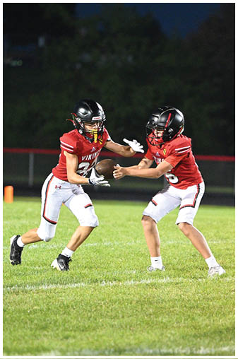 Two football players in red and white uniforms playing on a field. Description generated by AI