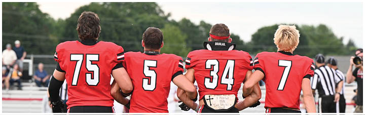 Four football players standing on the field. Description generated by AI