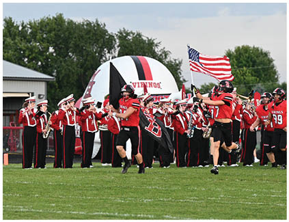 A group of people marching on a field with a flag. Description generated by AI
