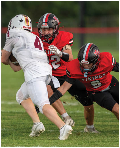 A football player in a white jersey is tackled by a player in a red jersey. Description generated by AI
