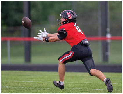 A football player wearing a red jersey with the number 4 on it catching a football. Description generated by AI