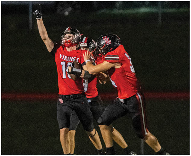 A group of men wearing red and black jerseys celebrating a touchdown. Description generated by AI