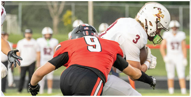 A football player in a red jersey is tackled by another player. Description generated by AI