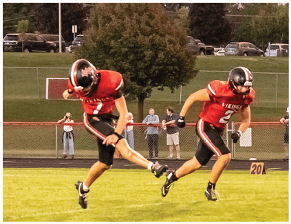 Two football players are running on a field. Description generated by AI