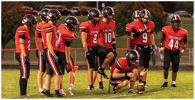 A football player kneeling on the ground with a football in front of him. Description generated by AI