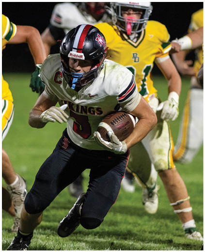 A football player in a black jersey is running with a football. Description generated by AI