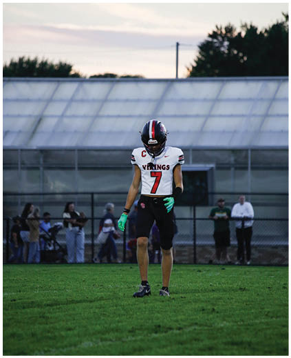 A young boy wearing a football uniform stands on a field. Description generated by AI