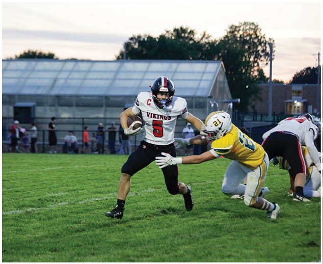 A football player in a white jersey with the number 5 on it is running with the ball. Description generated by AI