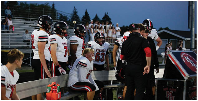 A group of football players sitting on a bench. Description generated by AI