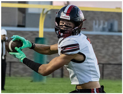 A football player wearing a white jersey and black shorts catching a football. Description generated by AI