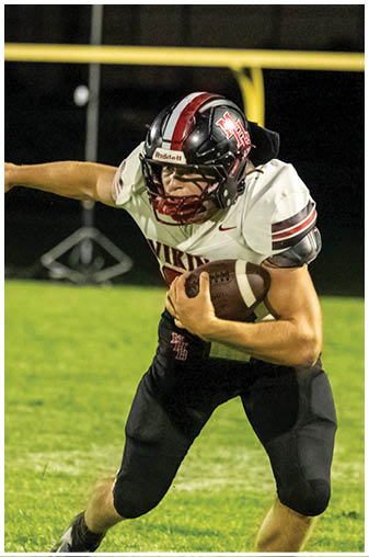 A football player in a black jersey running with a football. Description generated by AI