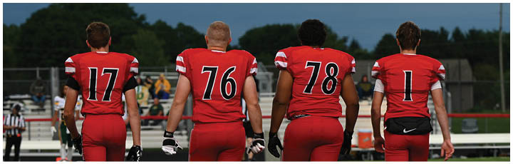 Four football players wearing red and black uniforms. Description generated by AI