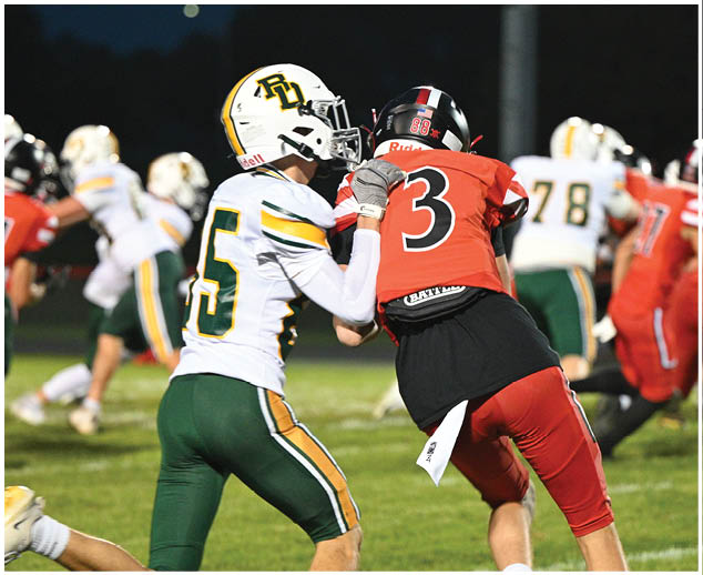 A football player in a red jersey is trying to block a player in a green and white jersey. Description generated by AI