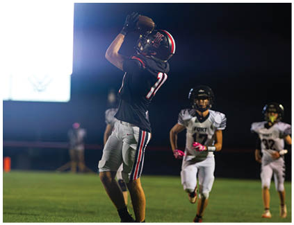 A football player wearing a white jersey and black shorts catching a football. Description generated by AI