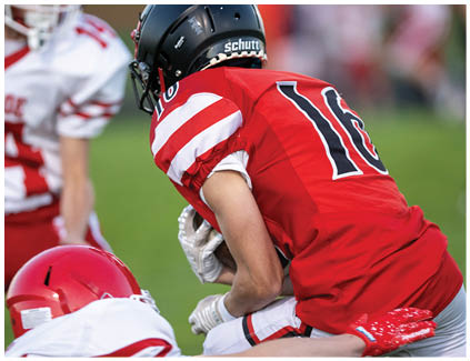 A football player wearing a white jersey and black shorts catching a football. Description generated by AI