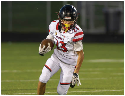 A football player wearing a white jersey and black shorts catching a football. Description generated by AI