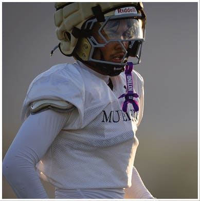 A person wearing a white football jersey and gloves is standing outdoors in soft lighting. Description generated by AI