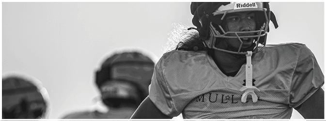 Three people wearing football helmets and jerseys stand together, with one person in the foreground showing the name “MUEL" on their jersey. Description generated by AI