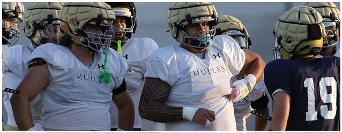 Several people wearing football uniforms stand together, with some resting their hands on their hips. Description generated by AI