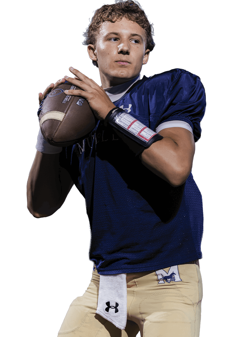 A person wearing a dark blue sports jersey is holding a football in a throwing position with a wrist coach on one arm. Description generated by AI