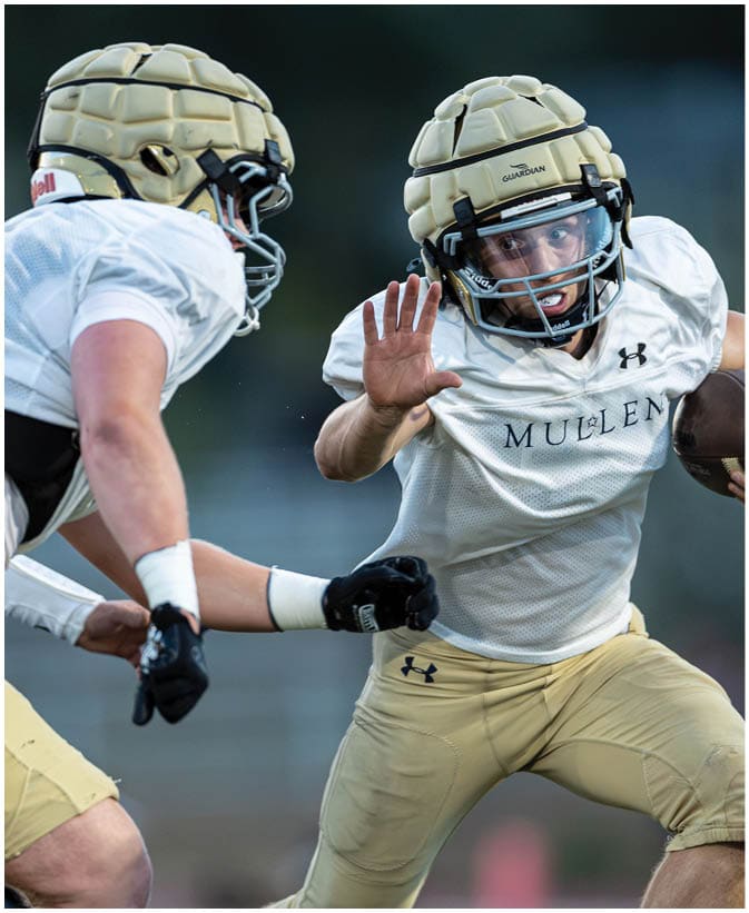 Two people wearing padded helmets and sports uniforms are engaged in an intense moment during a football practice or game. Description generated by AI
