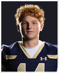 Person with curly hair wearing a dark sports jersey with gold trim is shown against a black background. Description generated by AI