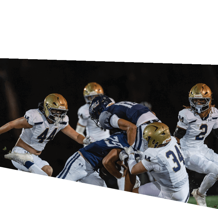 Four people in football uniforms are engaged in a tackle during a nighttime game on a grassy field. Description generated by AI
