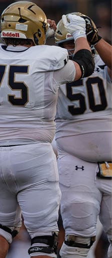 Two people wearing white sports uniforms are engaged in a football play on a field. Description generated by AI