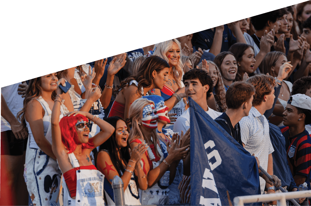 A large group of enthusiastic people wearing casual and patriotic clothing are gathered closely together, cheering and clapping at an outdoor event. Description generated by AI