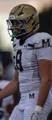 A person wearing a white football uniform with the number 8 and a gold helmet is standing on a field. Description generated by AI
