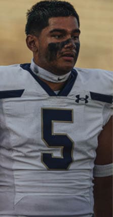 A person wearing a white football uniform with the number 5 and black face paint is standing on a field. Description generated by AI