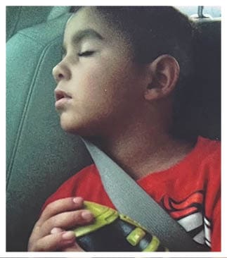 A child wearing a red shirt is sleeping while secured with a seatbelt. Description generated by AI
