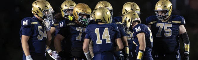 A group of people wearing dark athletic uniforms and gloves are standing closely together on a field. Description generated by AI