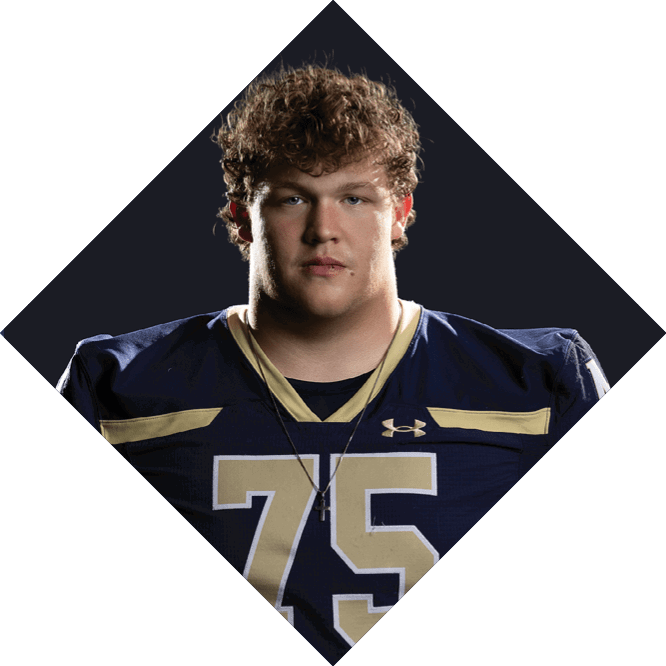A person with curly hair wearing a dark blue and gold football jersey with the number 75 stands against a dark background. Description generated by AI