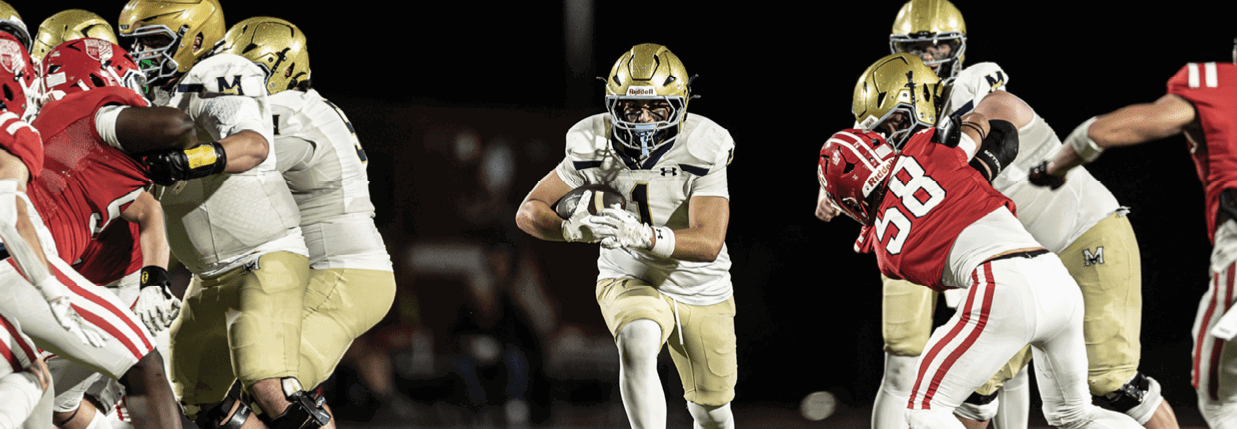 Adults wearing football helmets and uniforms are engaged in a game on a field at night. Description generated by AI