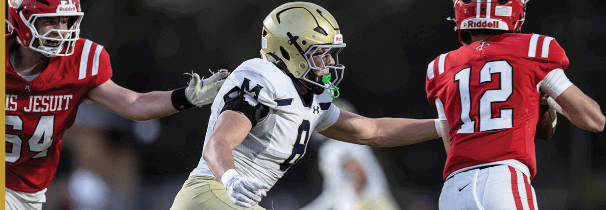 Three people wearing football helmets and uniforms are engaged in a play on a field with a blurred background. Description generated by AI